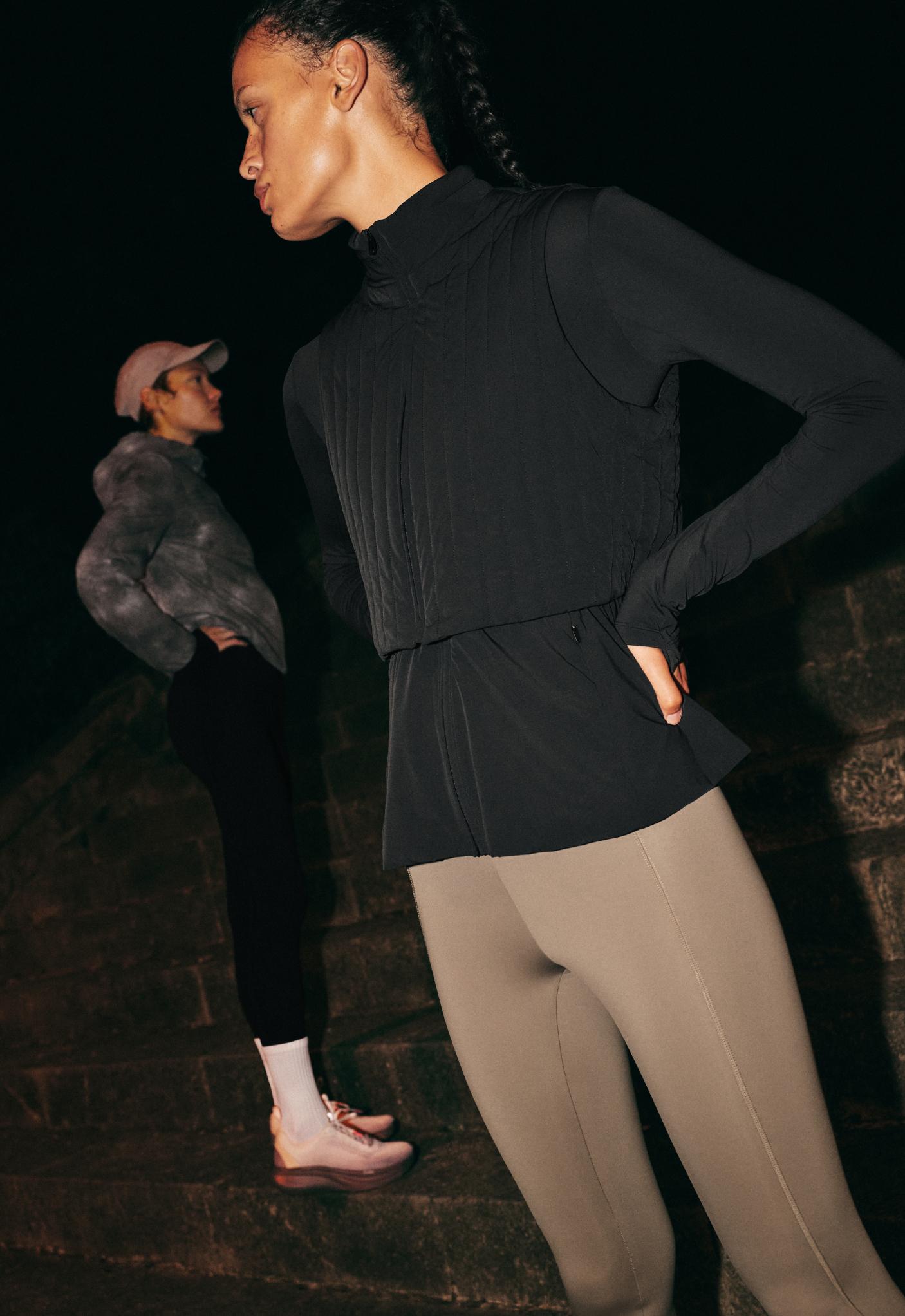 Black outfit featuring a high-neck jacket with a layered design and long sleeves with thumbholes, paired with gray leggings with seams.