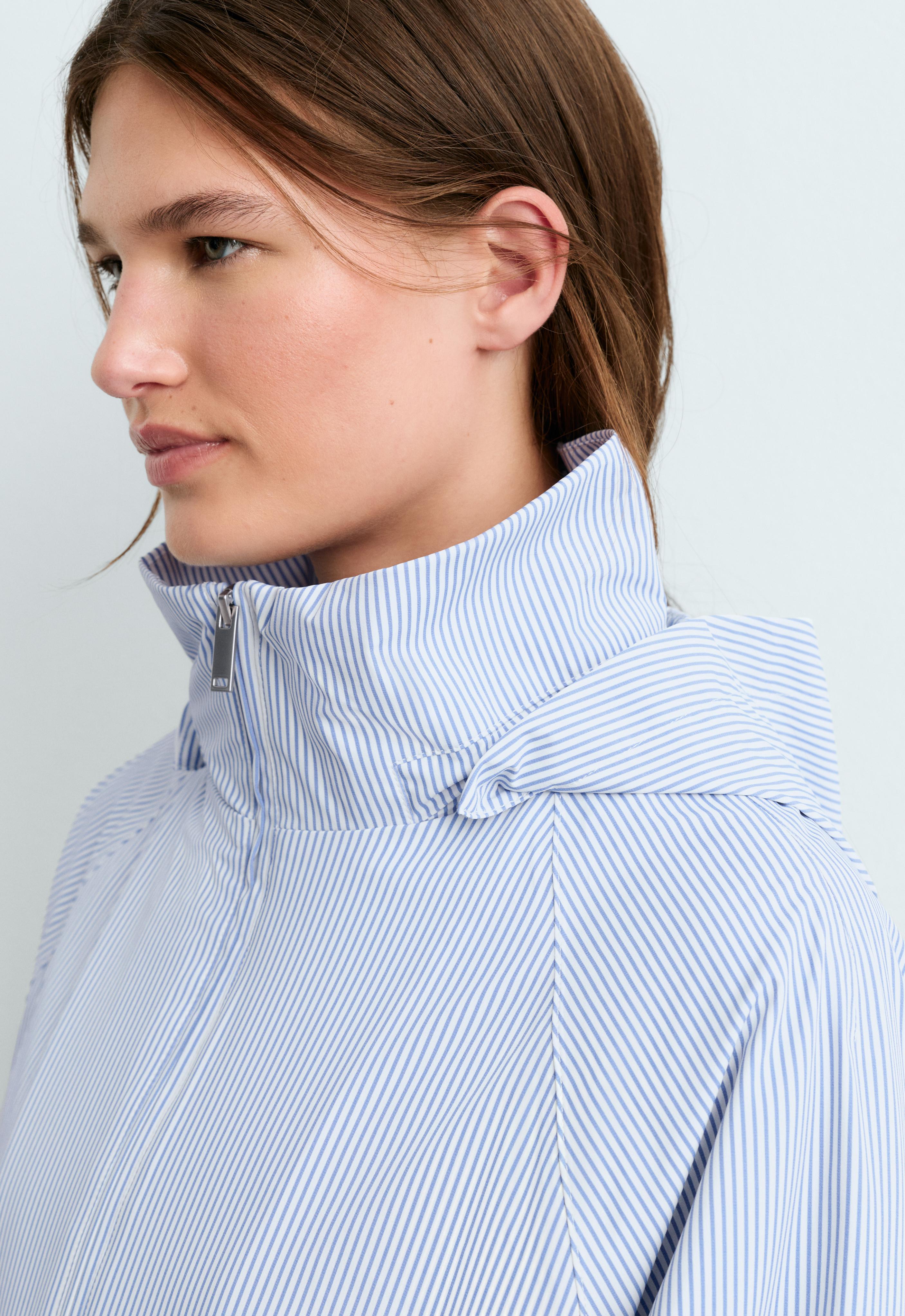Close-up of the high collar and hood of a light blue jacket with white stripes and a front zipper closure.