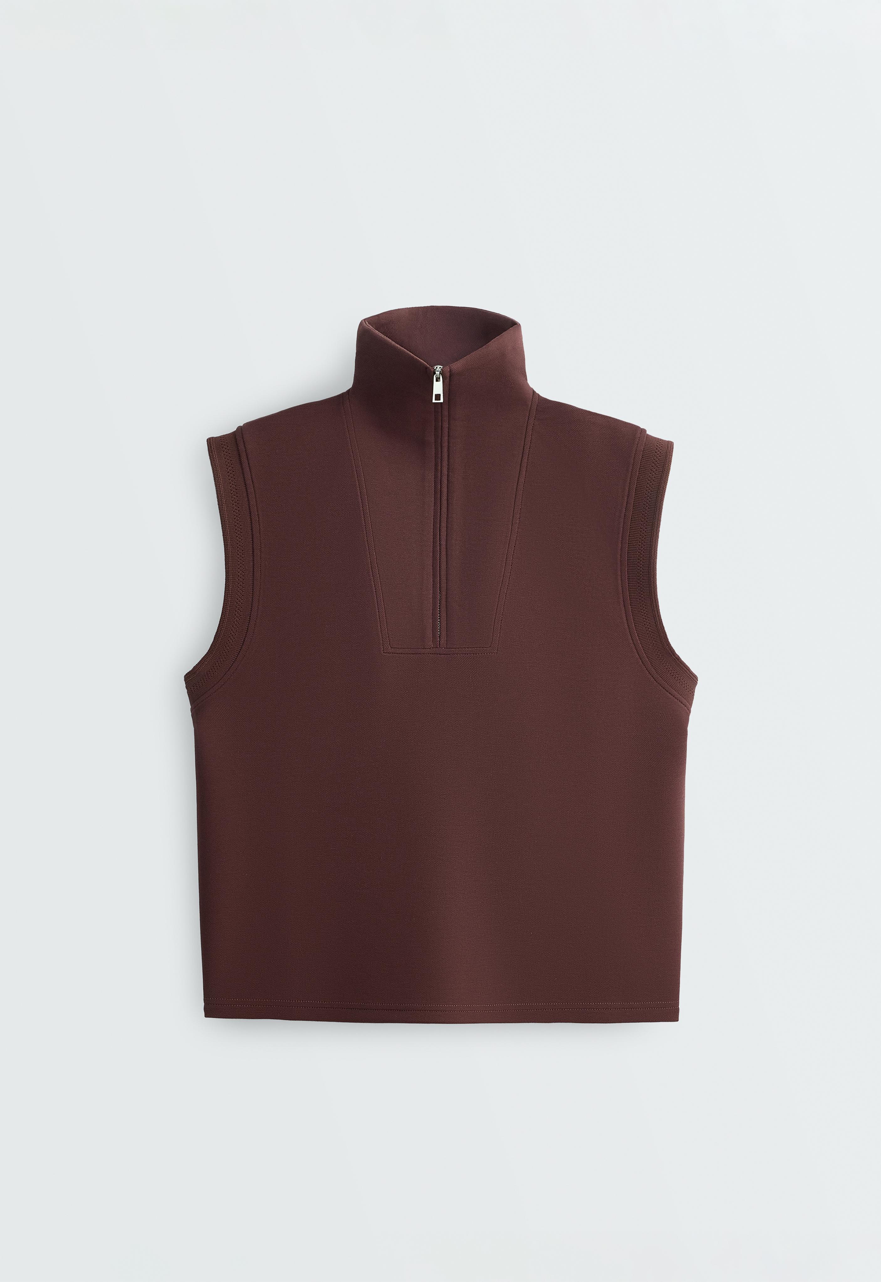 Front view of a chocolate-colored vest with a stand-up collar, sleeveless design, and front zipper closure. The chest seams stand out.