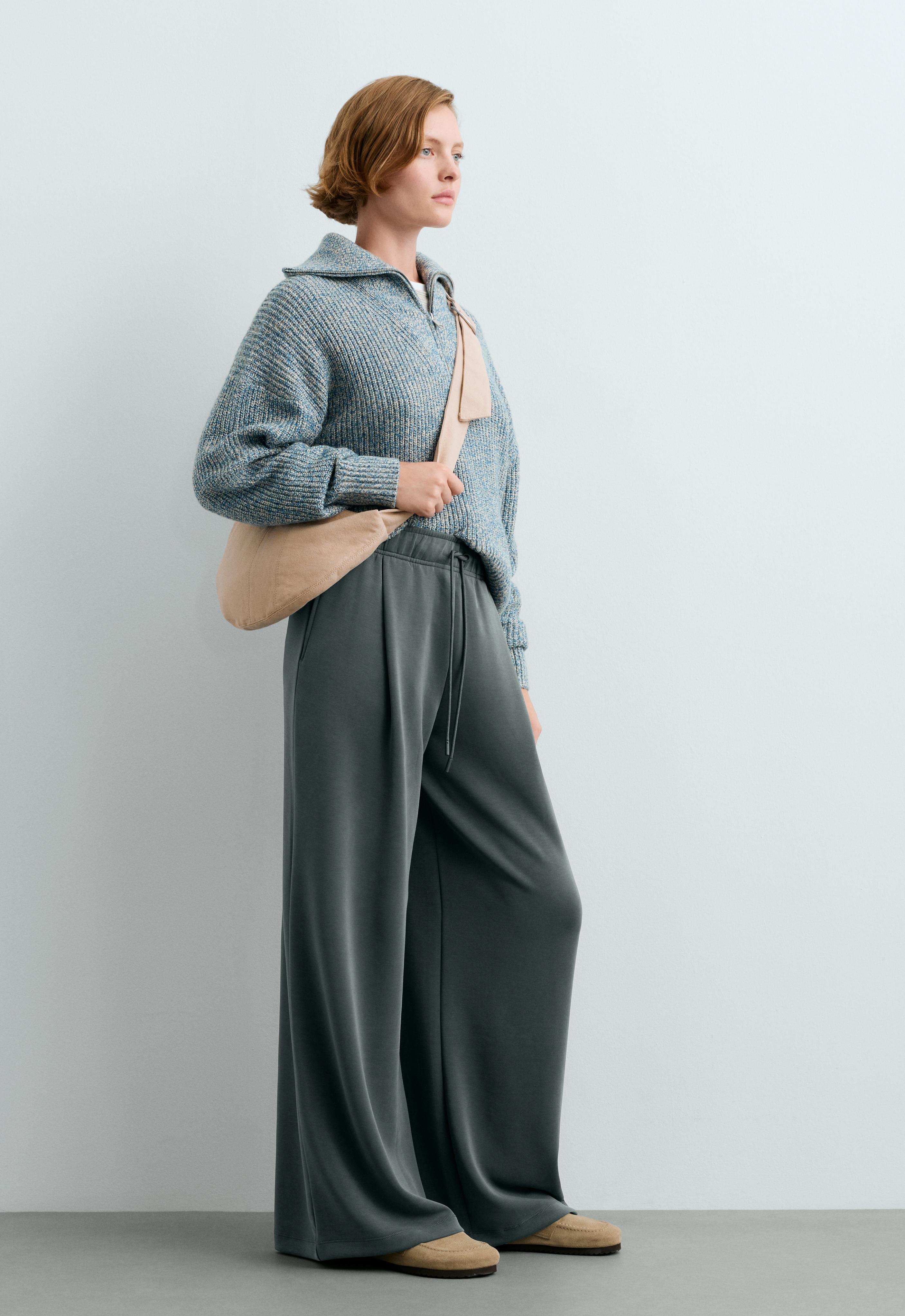 Dark gray wide-leg pants set with an elastic waistband, drawstring, pleats, and side pockets, knit sweater, and beige handbag.