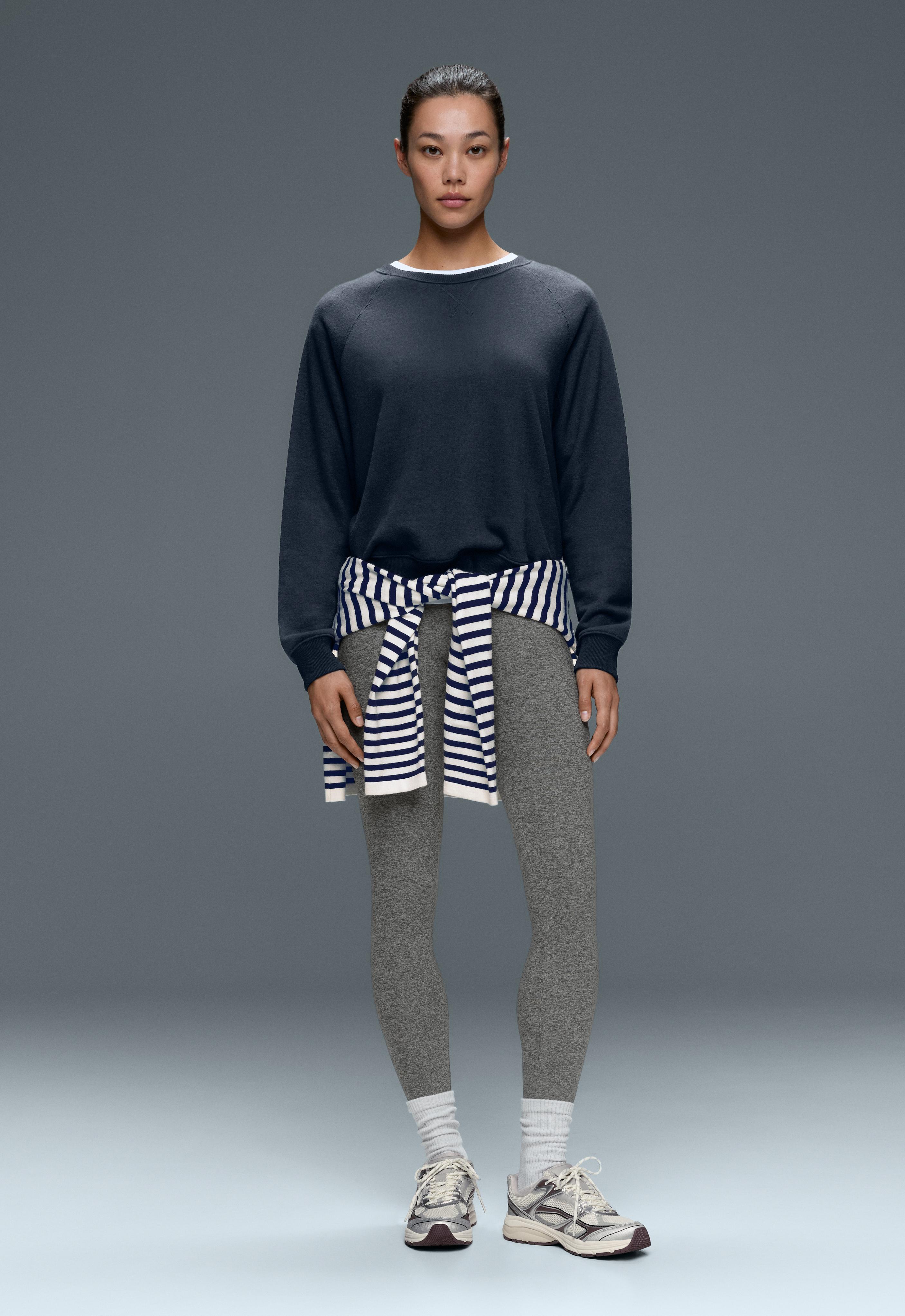 Dark blue sweatshirt set, white-and-blue striped sweater tied around the waist, fitted gray leggings, and sneakers.