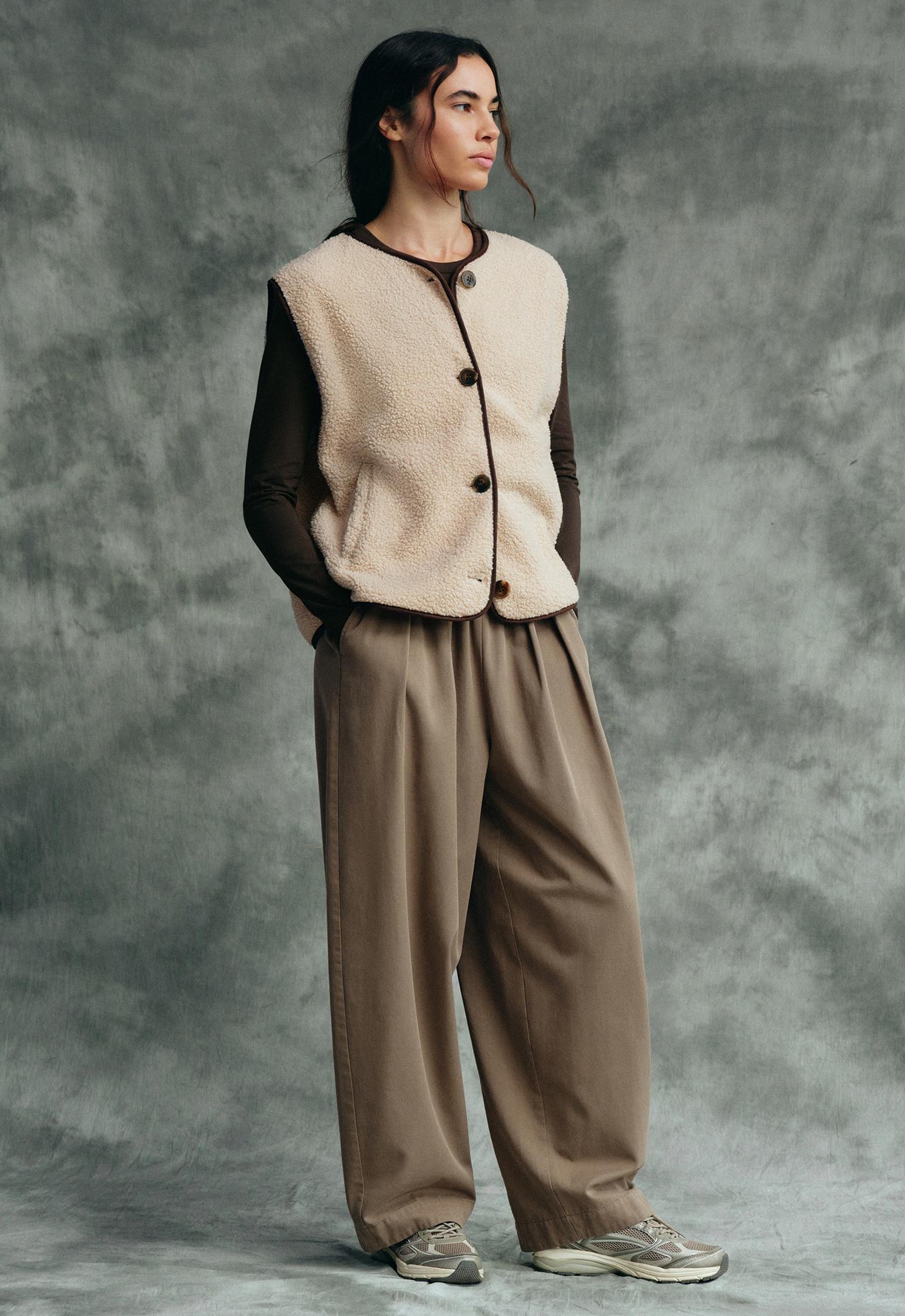 Beige button-up vest set, brown long-sleeve shirt, pleated khaki pants, and sneakers.