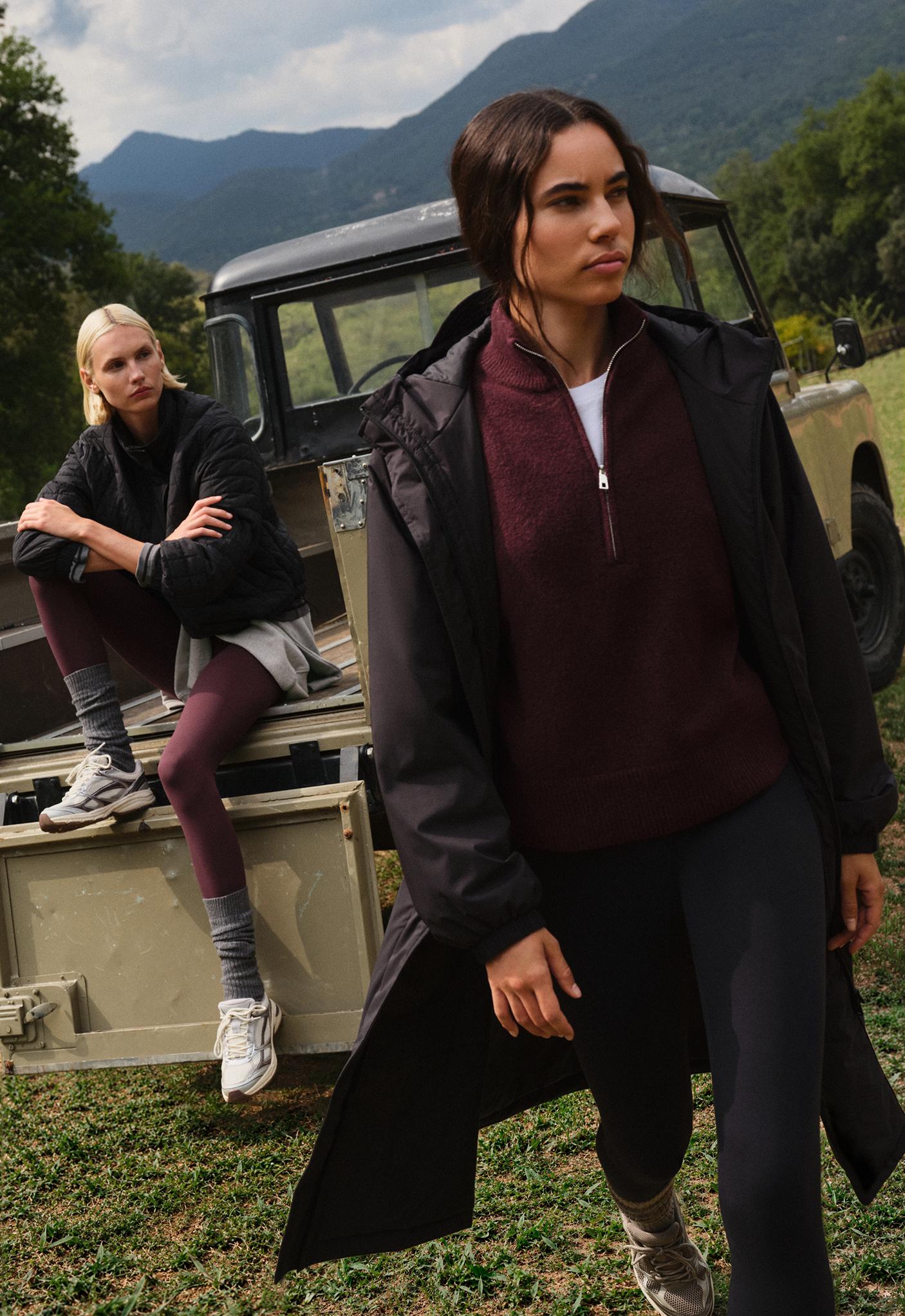 Set consisting of a long black hooded jacket with elastic cuffs, a burgundy turtleneck sweater with a half-zip, and black leggings.