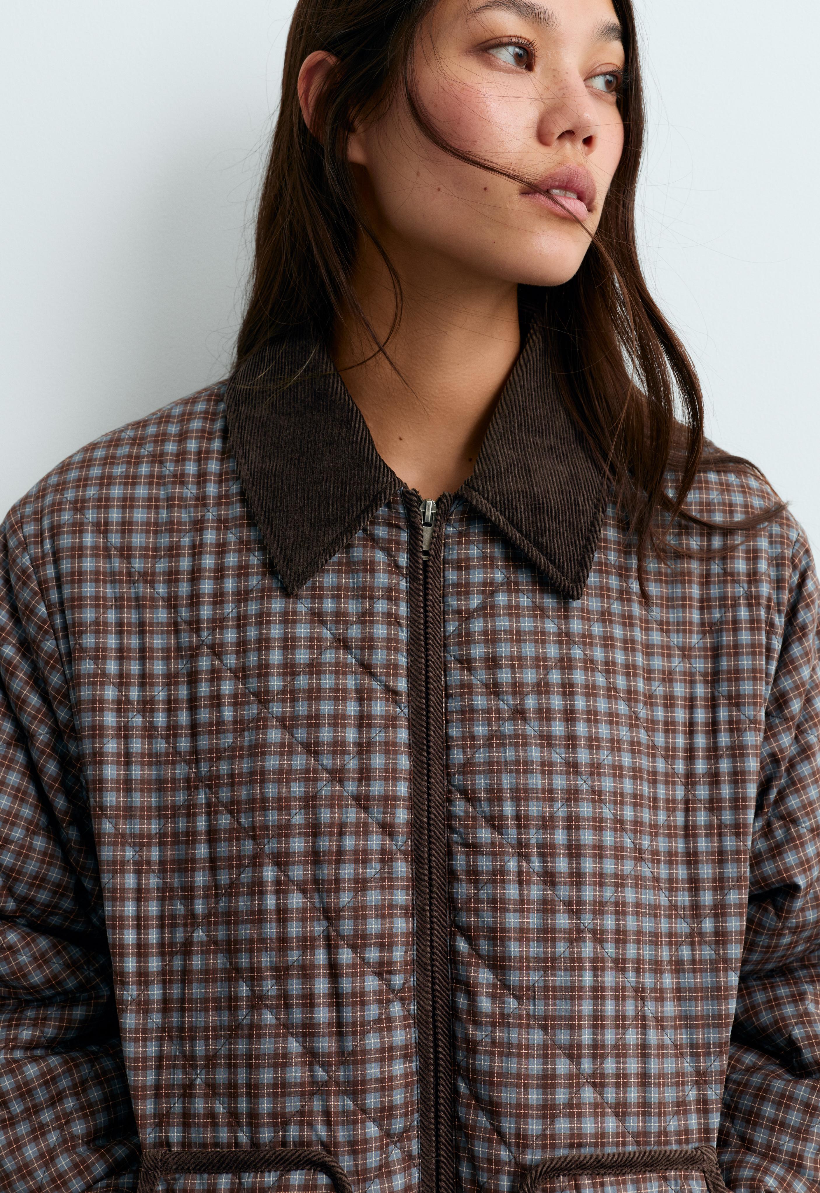 Medium shot of a plaid quilted jacket with diamond stitching, a dark brown collar, and a front zipper closure.