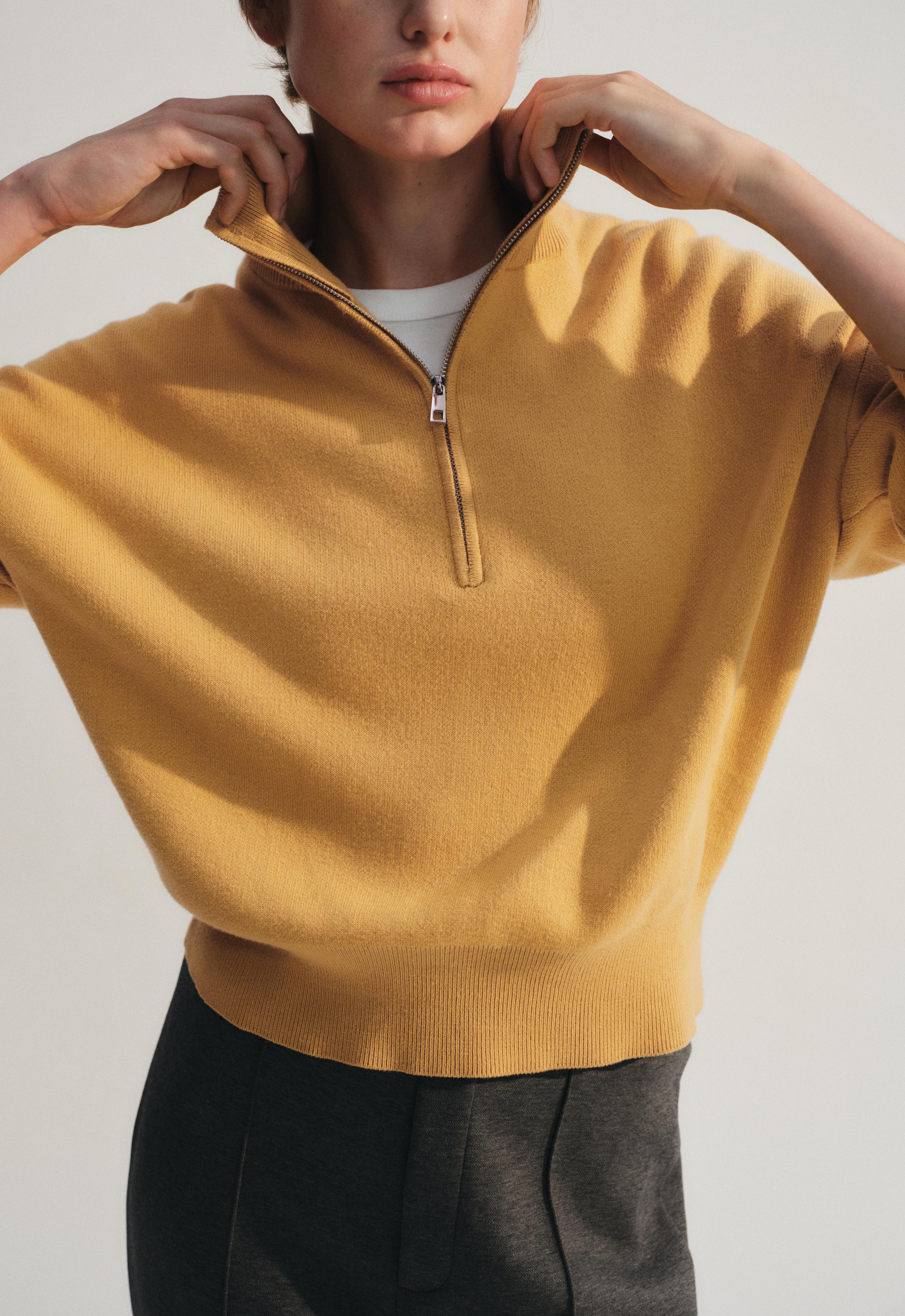 Medium shot of an ochre turtleneck sweater with a half-front zipper, long sleeves, and a ribbed hem.