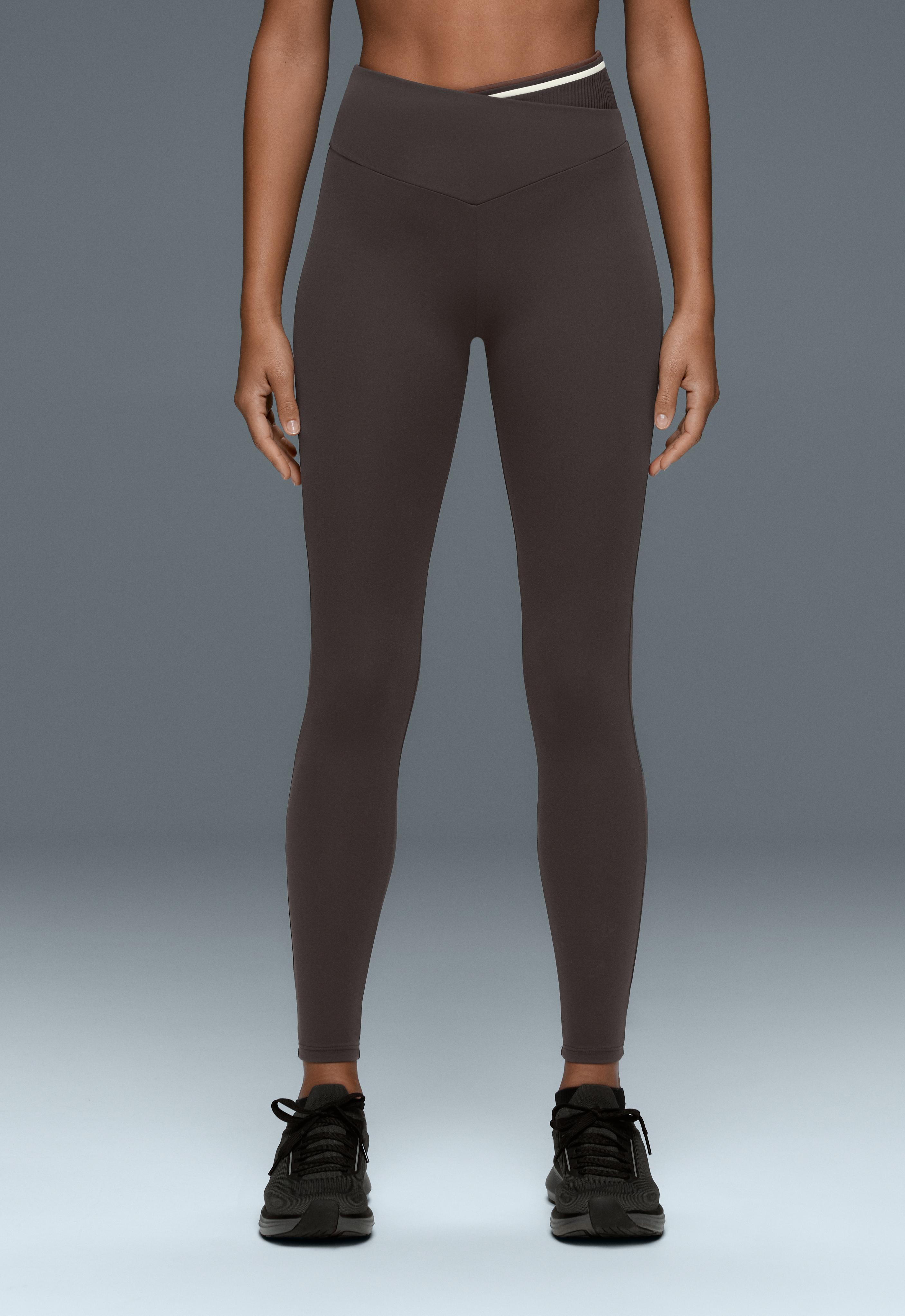 Dark gray leggings set with a V-shaped crossover waistband, white trim, and ankle length, paired with black sneakers.