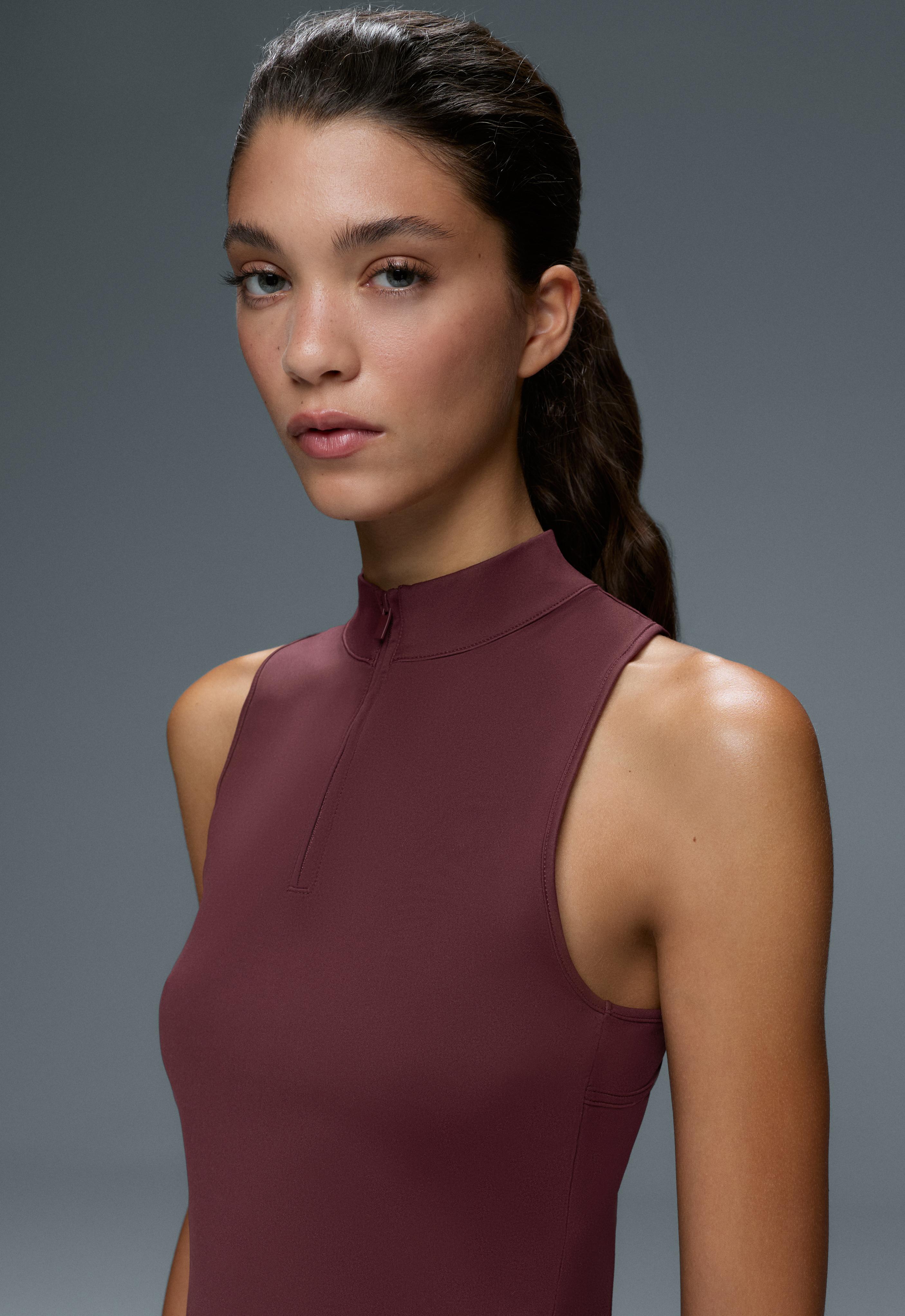 Close-up of a fitted sleeveless burgundy top with a high neck and front half-zip closure.