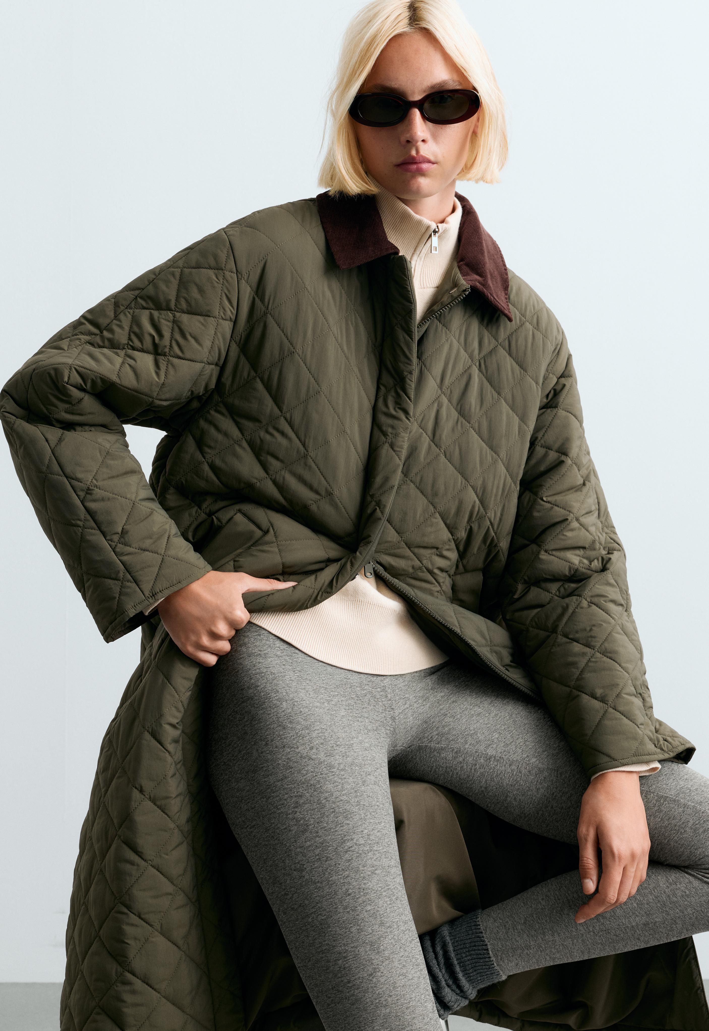 Set consisting of a long quilted khaki jacket with a diamond pattern and contrasting collar, a light-colored sweater, and gray leggings.