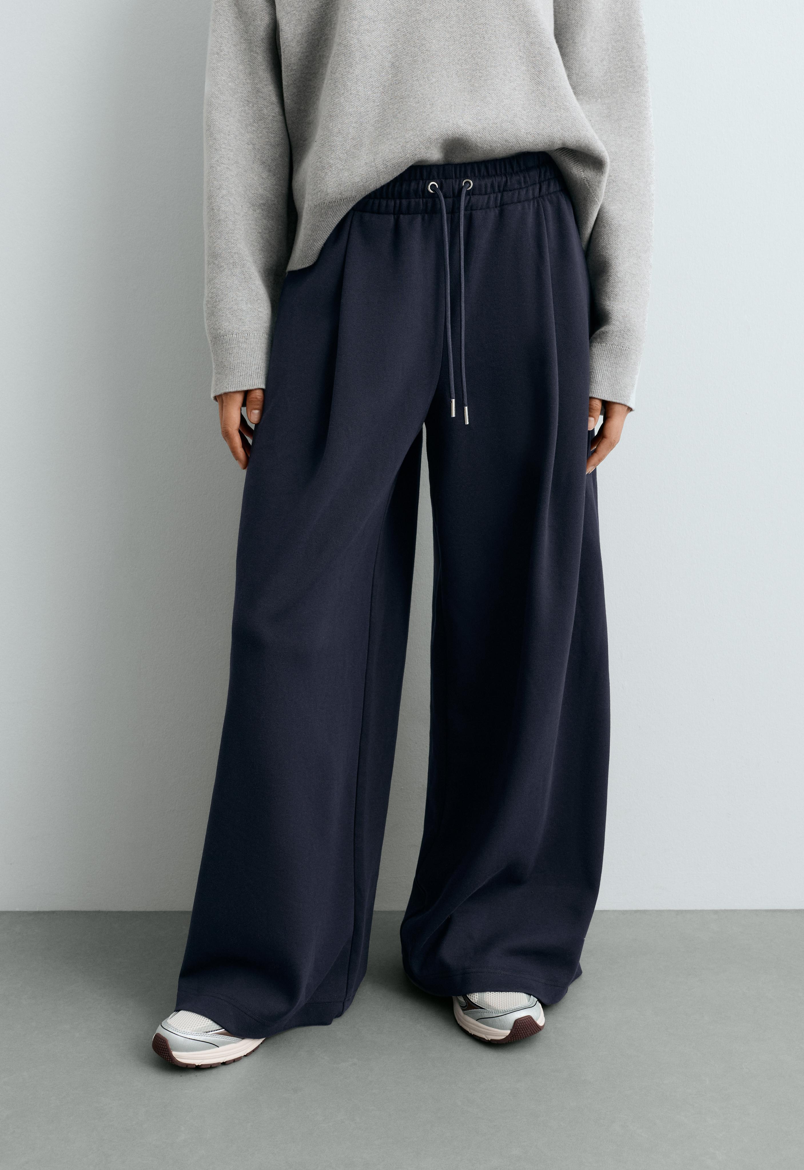 Gray jersey set, wide-leg dark blue pants with an elastic waistband, drawstring, and pleats, and sneakers.