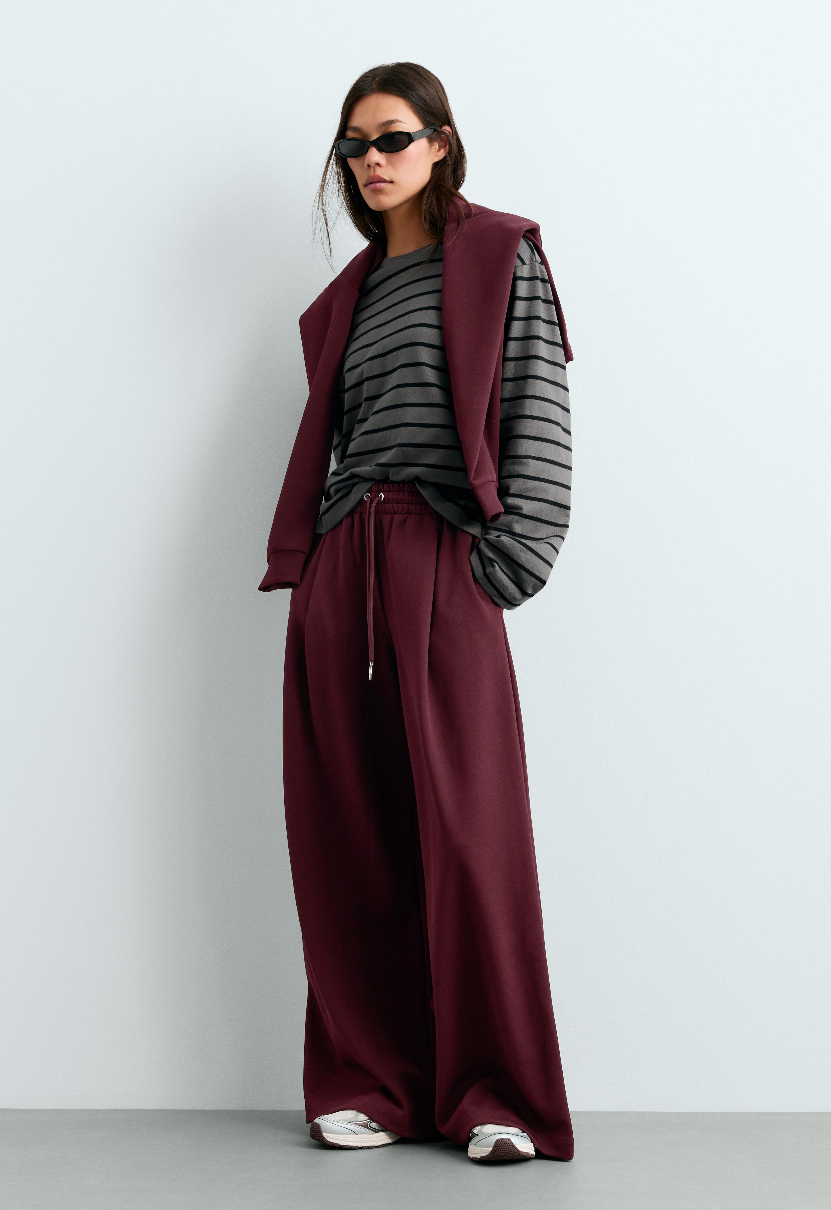 Burgundy wide-leg pants set with an elastic waistband, drawstring, and pockets, striped T-shirt, and sweater draped over the shoulders.