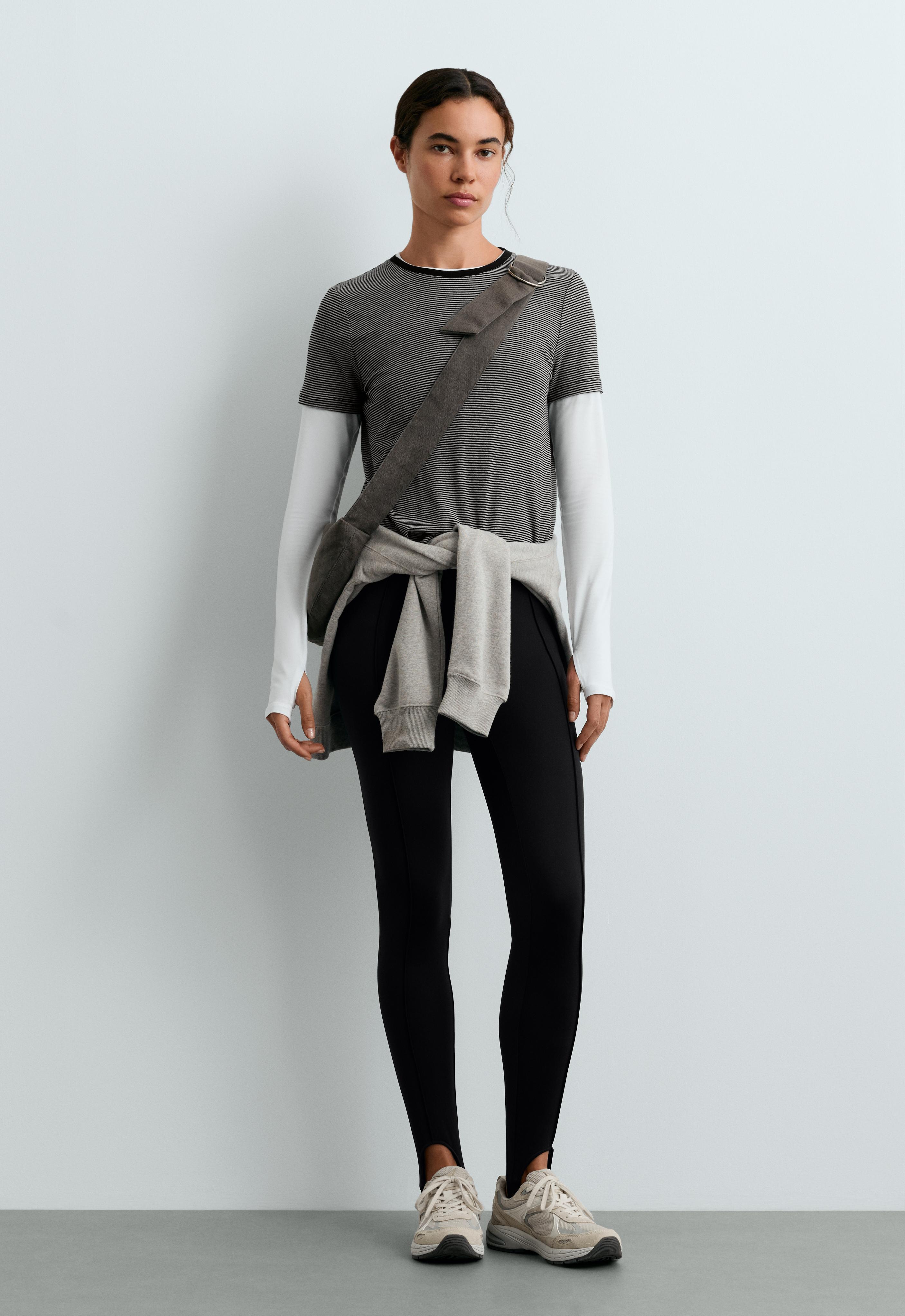 Set of black leggings with a front seam and elastic under the foot, striped T-shirt, sweatshirt tied around the waist, and sneakers.
