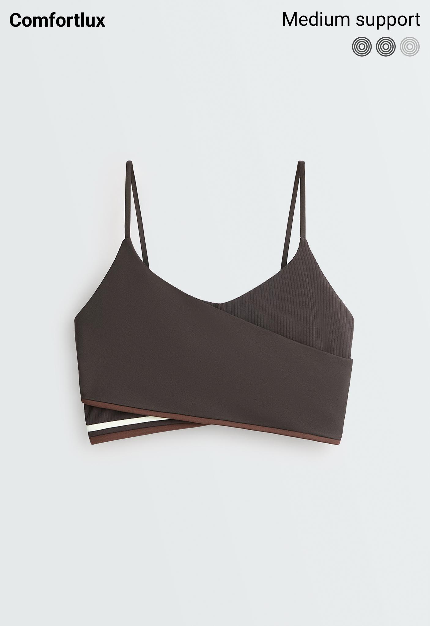 Front view of a dark gray sports bra with thin straps, a crisscross design, ribbed texture, and a contrasting striped hem.