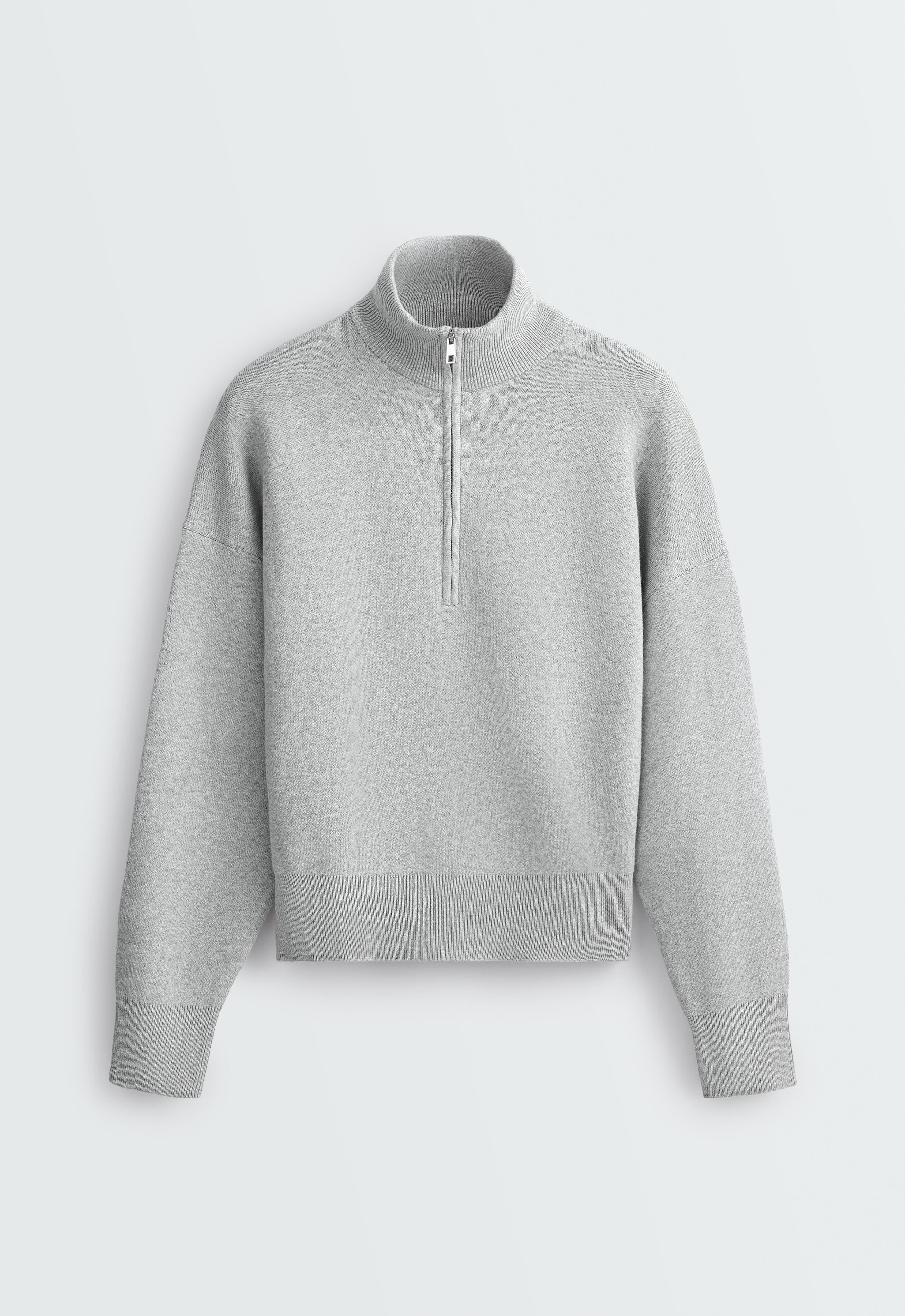 Front view of a light gray long-sleeve sweater. It features a high neck with a half-zipper and ribbed details on the collar, cuffs, and hem.