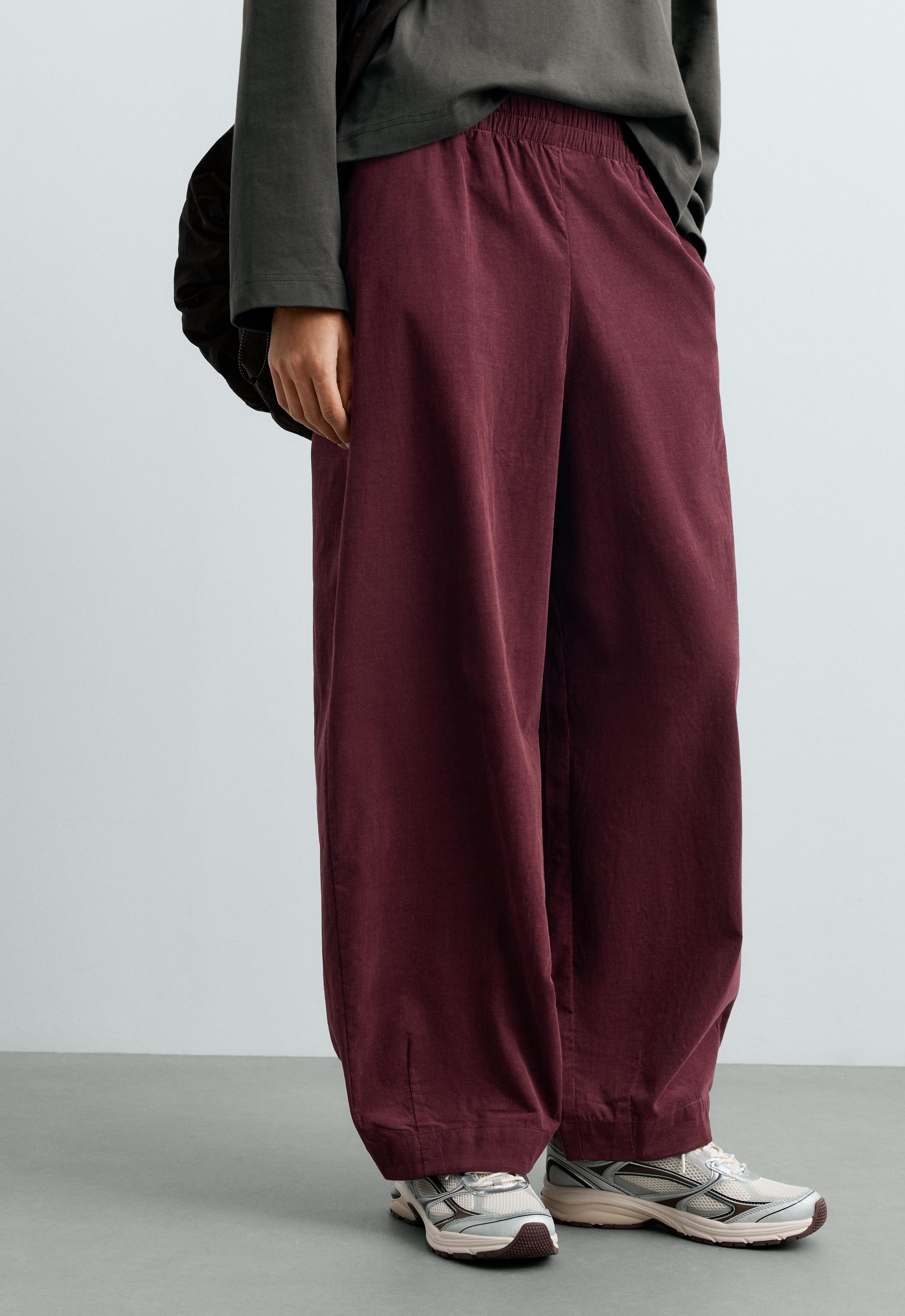 Medium shot of burgundy balloon-cut pants with an elastic waistband and side pockets.